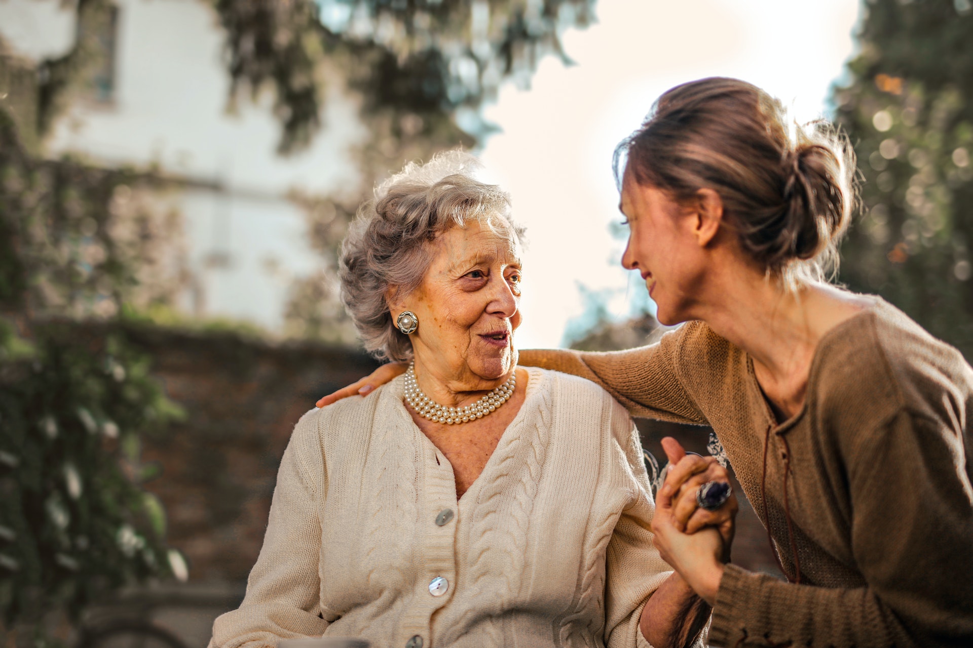 A woman sits with her arm around an elderly woman as they talk