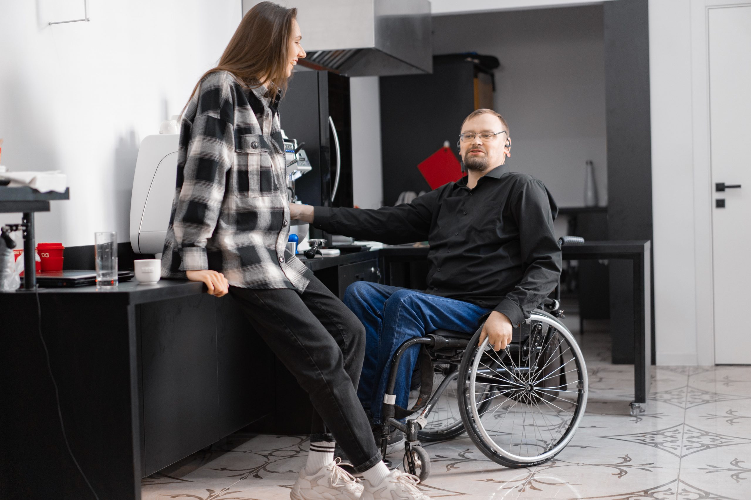 A woman leans against a cabinet while talking with a man in a wheelchair