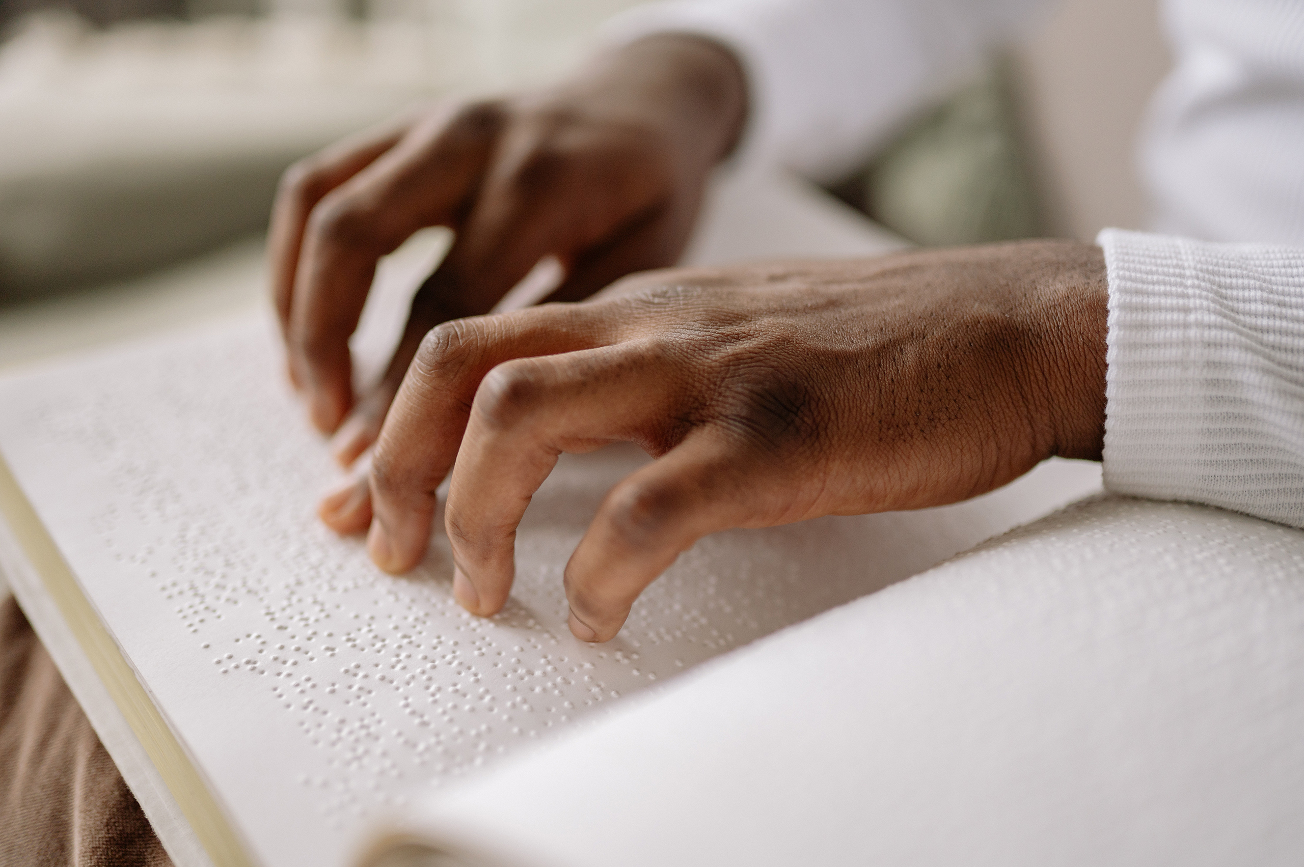 Close up photo of a man's hands reading a Braille book
