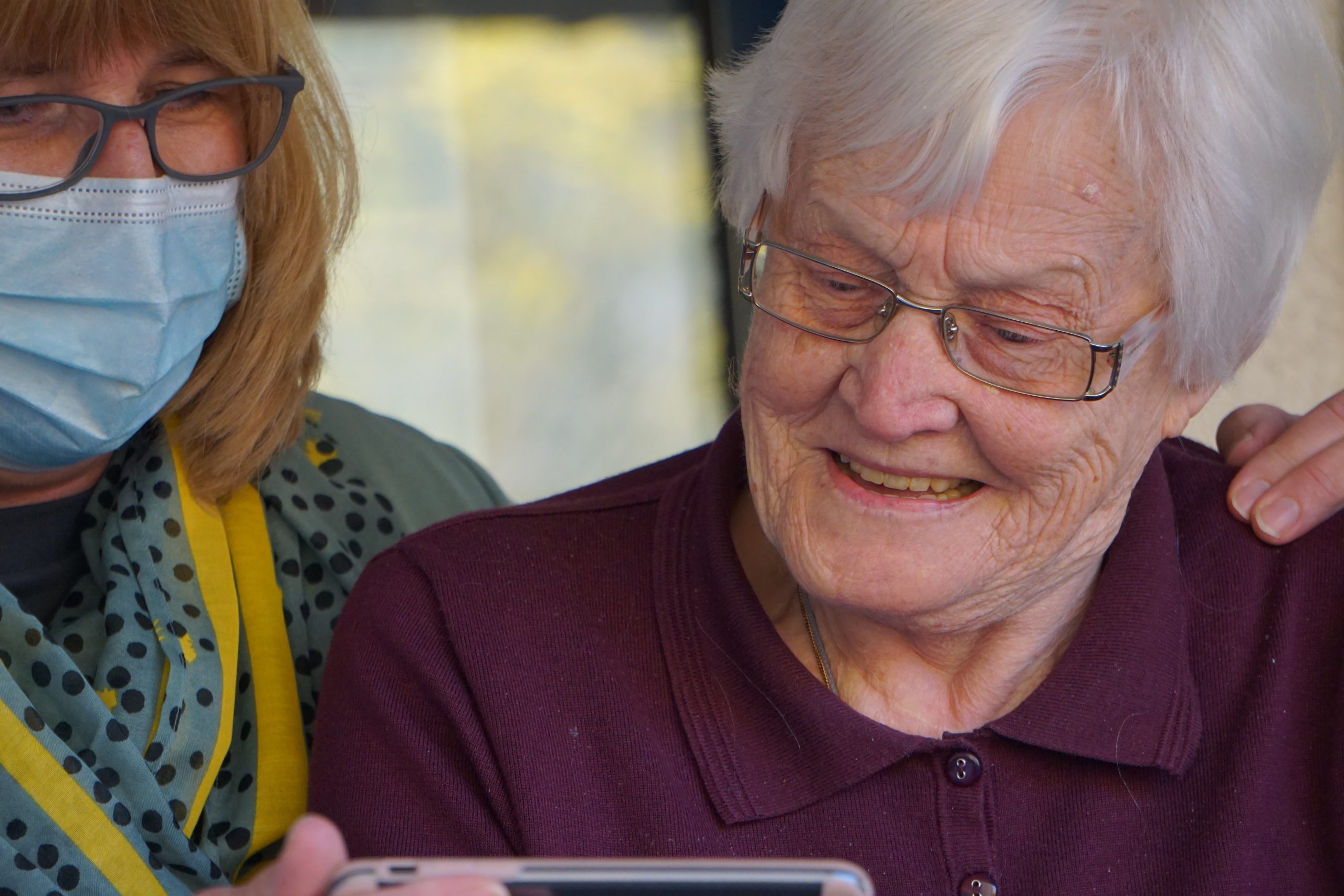 A home health aide looks at a phone with an elderly woman