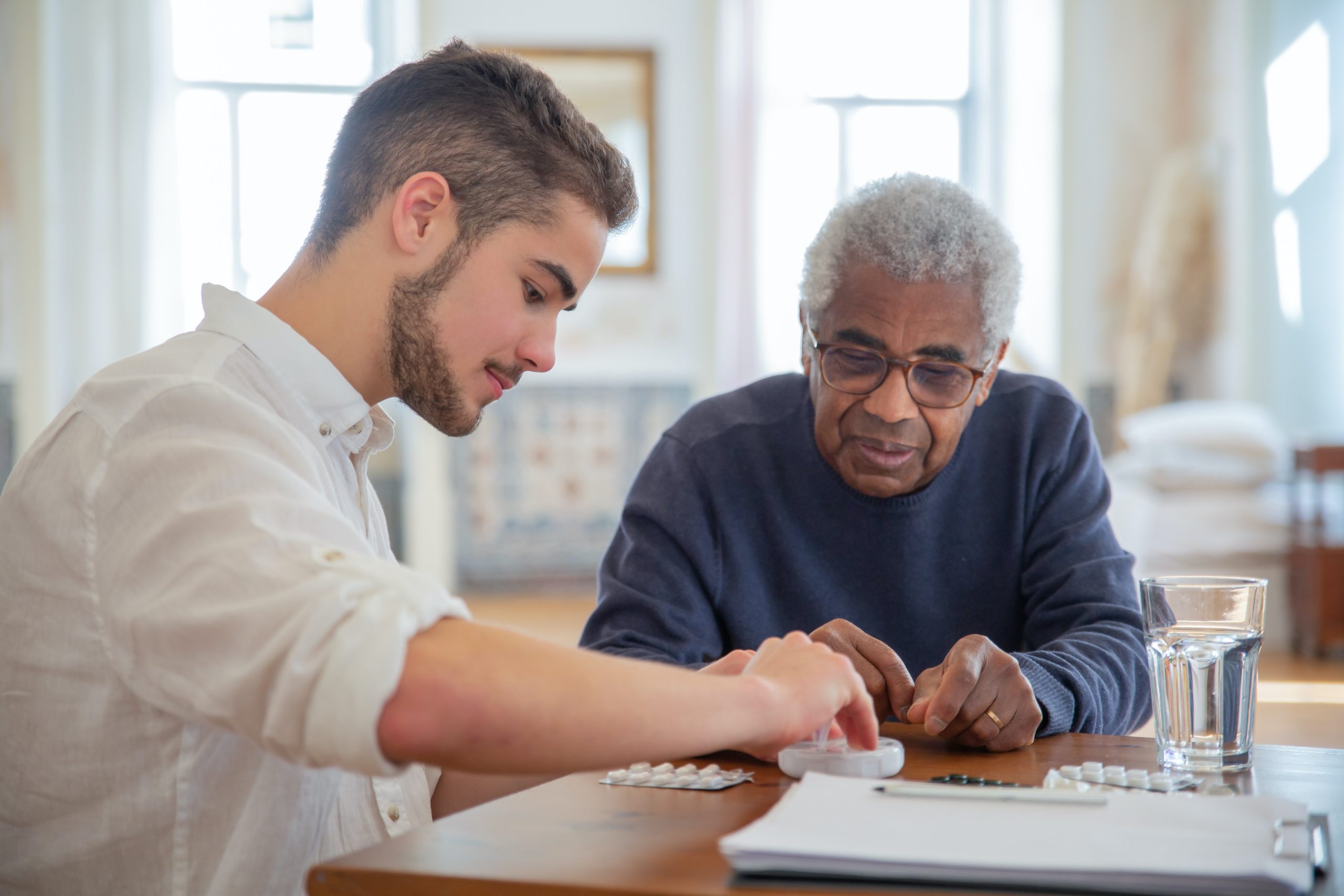 A man sorts medication at a table with an elderly man